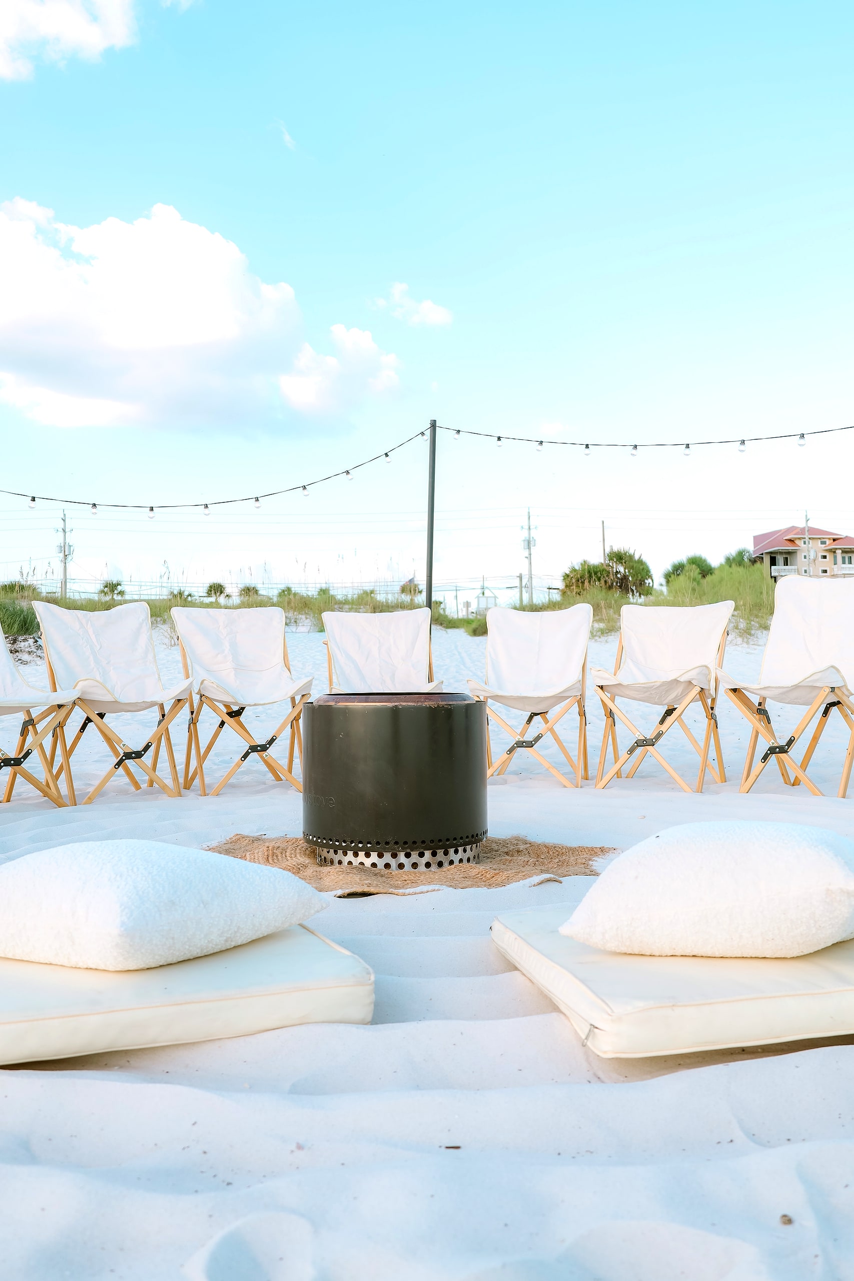 Sling chairs and bouclé floor cushions beneath string lights