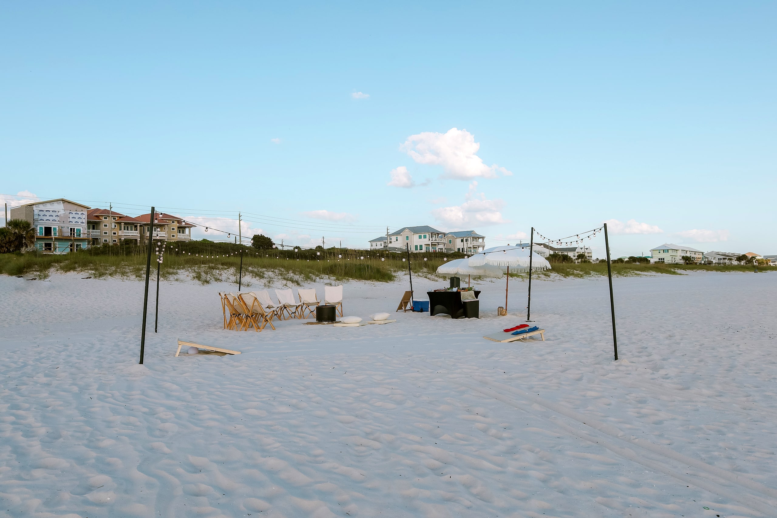 A full circle of styled beach chairs around a fire pit with spiral sand art, seating a large group on the white sand